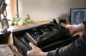Un artiste 3D découvre une RTX 5090 signée par Jensen Huang Un artiste 3D déballe une carte graphique RTX 5090 noire avec une signature dorée de Jensen Huang sur son bureau.