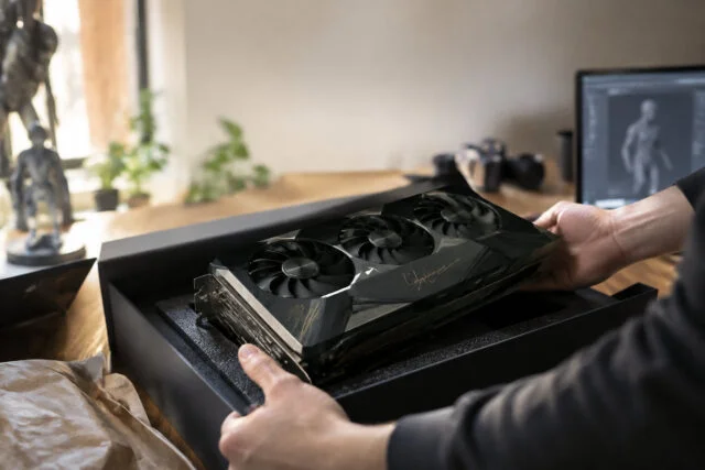 Une RTX 5090 dédicacée par Jensen Huang Un artiste 3D déballe une carte graphique RTX 5090 noire avec une signature dorée de Jensen Huang sur son bureau.