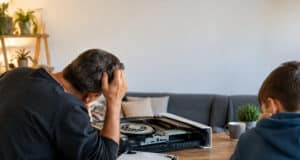 Un père et son fils examinant une console PS5 démontée sur une table en bois, l'homme semble perplexe.