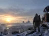 Un survivant en équipement hivernal observe les ruines d'une ville enneigée au lever du soleil sur une voie ferrée.