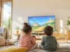 Nintendo lance deux jeux Mario gratuits sur Switch et Switch 2 Deux enfants assis au sol dans un salon lumineux, jouant à un jeu vidéo Mario sur une grande télévision.