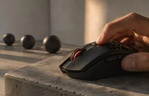 Une main utilise une souris gaming noire avec un éclairage rouge sur un socle en béton sous une lumière naturelle.