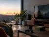 Manette Xbox et boîtiers de jeux sur une table basse, devant une télévision et un coucher de soleil.