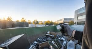 Une personne porte des gants de travail et tient un processeur et de la mémoire vive extraits d'une benne à déchets.