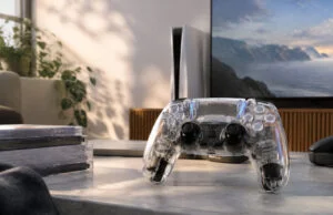 Une manette DualSense transparente posée sur une table devant une console PS5, évoquant le design des années 90.
