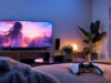 Ecchi Memories gratuit sur PS4 et PS5 : un Platine rapide Une manette PS5 posée sur un lit face à une télévision diffusant un paysage animé au coucher du soleil dans un salon.