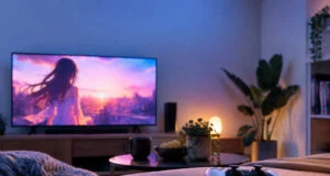Une manette PS5 posée sur un lit face à une télévision diffusant un paysage animé au coucher du soleil dans un salon.