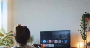 Une femme assise sur un canapé jouant à un jeu vidéo devant une télévision dans un salon confortable.