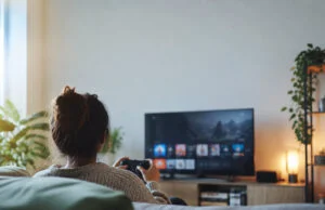 Comment annuler un abonnement gaming facilement Une femme assise sur un canapé jouant à un jeu vidéo devant une télévision dans un salon confortable.