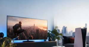 Une console PlayStation 5 et sa manette DualSense devant une télévision affichant le jeu Spider-Man.