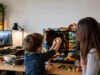 Un garçon de 5 ans crée un PC LEGO pour la Fête des Pères Un jeune garçon et une femme assemblent des briques LEGO autour d'un boîtier d'ordinateur sur un bureau en bois.