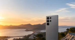Dos d'un smartphone Samsung Galaxy S26 Ultra posé sur un rocher face à un coucher de soleil sur une baie.