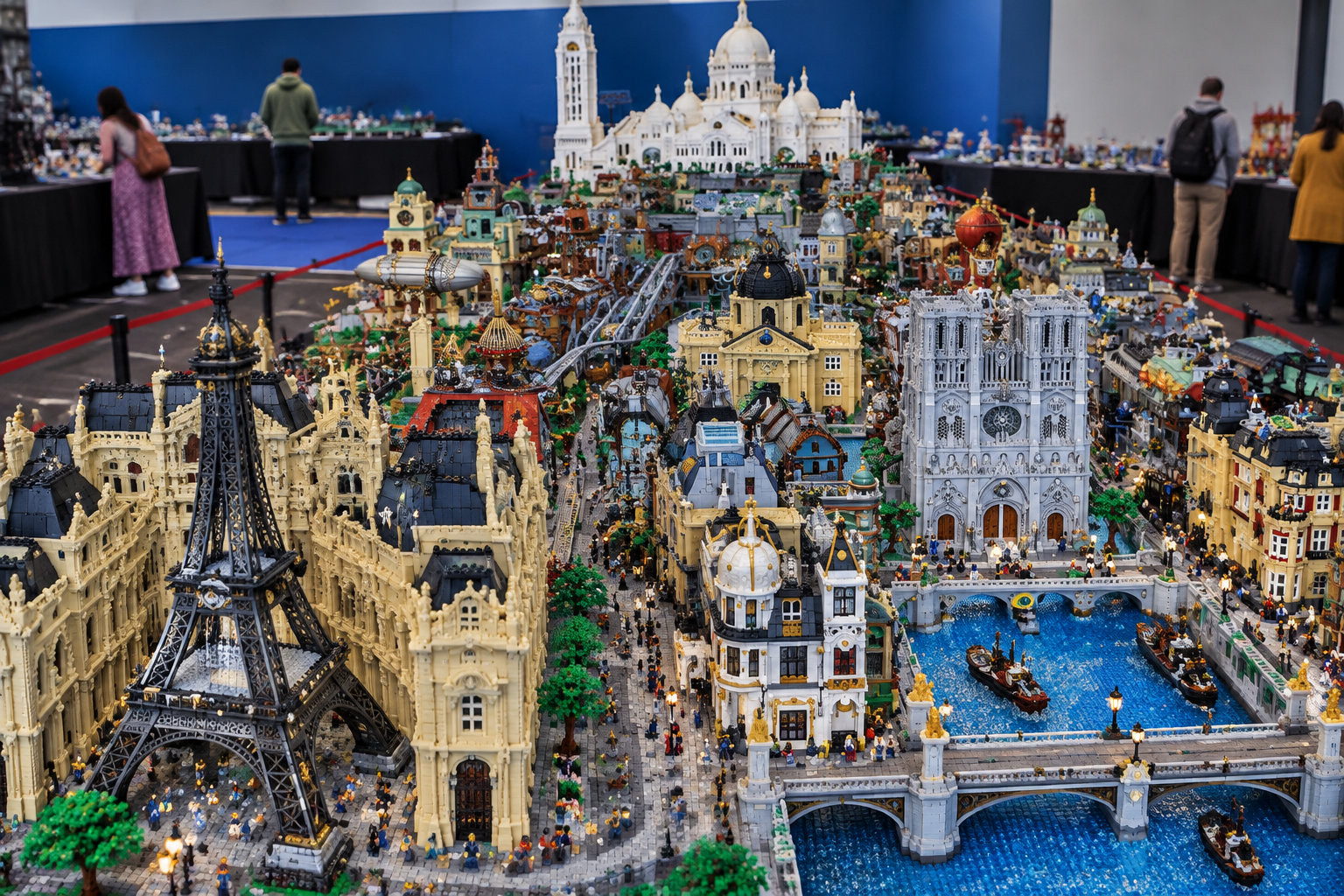 Une vaste maquette de ville composée de petites briques représente des monuments, des bâtiments, des rues et des canaux, observée par des visiteurs dans une salle d’exposition.