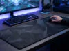 Tapis de souris XXL : l’accessoire qui va transformer votre aim Un joueur utilisant une souris sur un large tapis noir à motifs géométriques devant son écran et son clavier rétroéclairé.